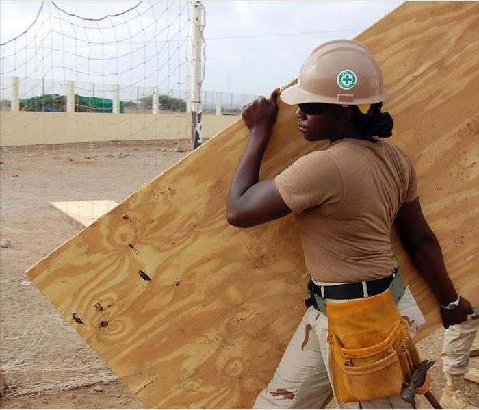woman carrying sheet of wood on construction site in appropriate gear